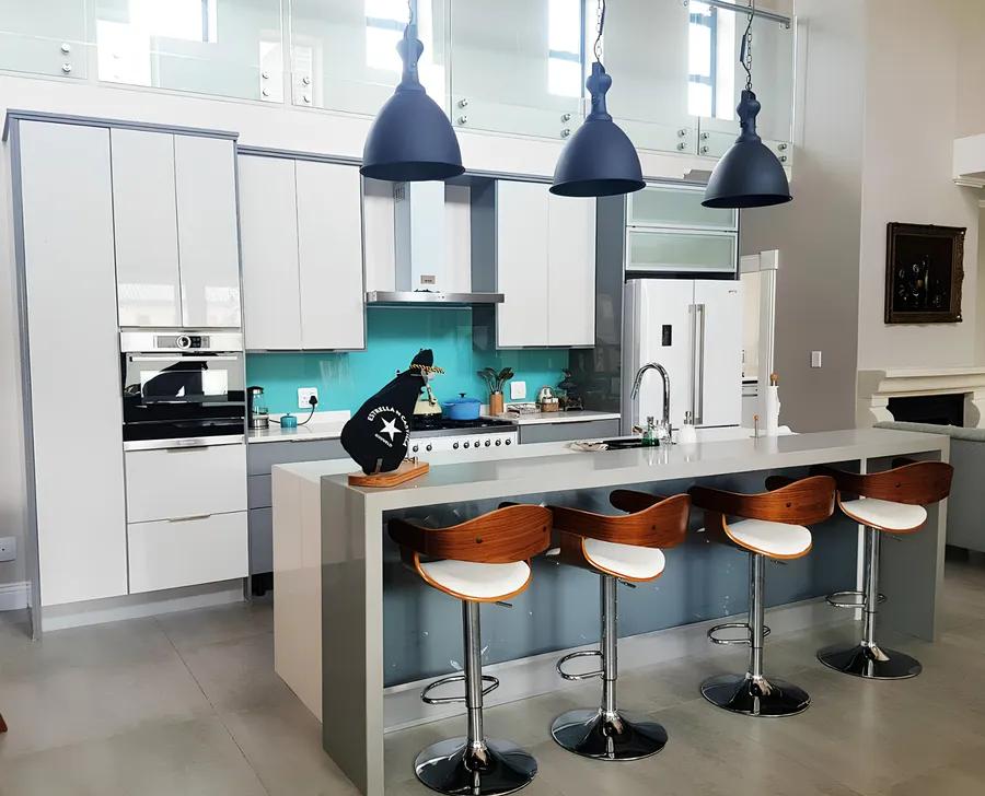 Double-volume kitchen with a teal glass splashback and island seating, fitted by N.D.I.